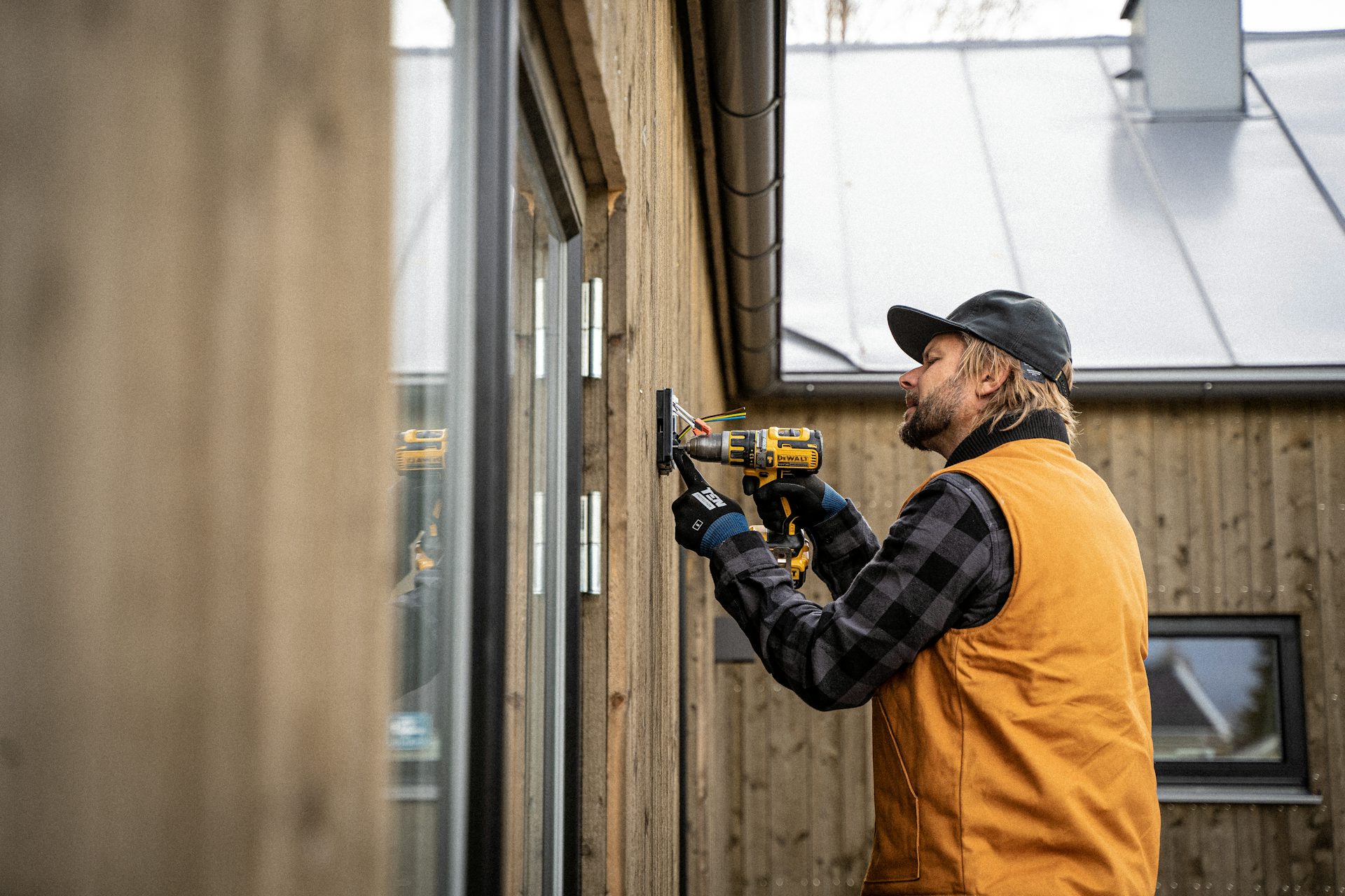 An electrician drilling a fixture onto the outside wall of a house